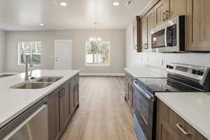 Kitchen with stainless steel appliances, light stone countertops, decorative light fixtures, light wood-type flooring, and recessed lighting