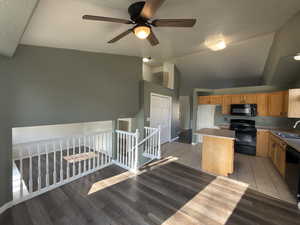 Kitchen with black appliances, light wood-style flooring, a ceiling fan, a center island, and light countertops