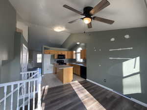 Kitchen featuring lofted ceiling, a kitchen island, black appliances, light wood-style floors, and light countertops