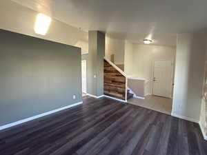 Empty room featuring lofted ceiling, dark wood finished floors, and stairway