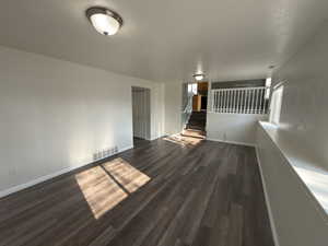 Unfurnished room featuring stairway and dark wood-style flooring