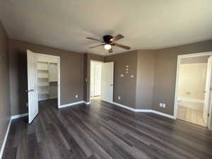 Unfurnished bedroom with a spacious closet, dark wood-type flooring, a textured ceiling, a ceiling fan, and ensuite bath