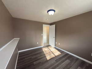 Empty room with dark wood-type flooring and a textured ceiling