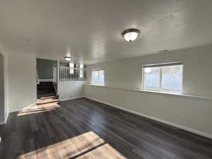 Unfurnished living room featuring dark wood-style floors, a textured ceiling, and stairs