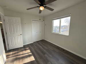 Unfurnished bedroom with dark wood-style flooring, a closet, and ceiling fan