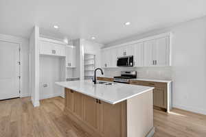 Kitchen featuring white cabinetry, stainless steel appliances, light wood-style flooring, a kitchen island with sink, and recessed lighting