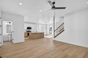 Unfurnished living room with stairs, a chandelier, recessed lighting, light wood finished floors, and ceiling fan