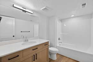 Bathroom featuring a textured ceiling, vanity, washtub / shower combination, and light wood-type flooring
