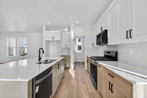 Kitchen with stainless steel appliances, an island with sink, white cabinetry, light wood finished floors, and recessed lighting