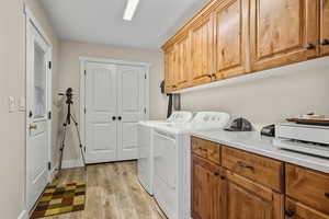 Laundry area featuring light wood-type flooring, washer and clothes dryer, and cabinet space