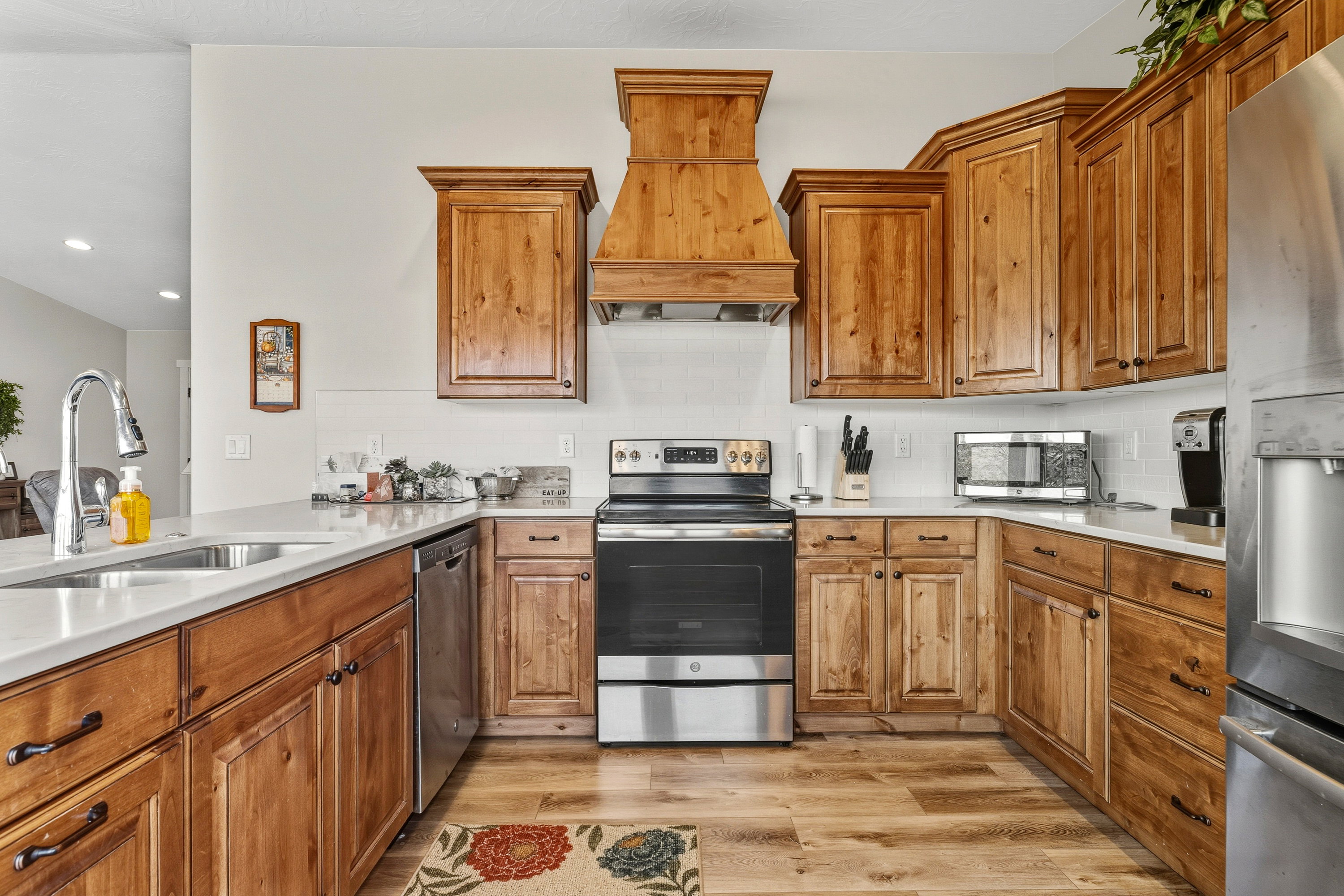 Kitchen with appliances with stainless steel finishes, premium range hood, brown cabinetry, light wood-style flooring, and backsplash