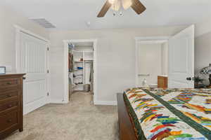 Bedroom with light carpet, a walk in closet, ceiling fan, and ensuite bathroom