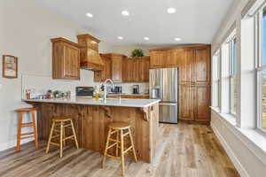 Kitchen with brown cabinets, a peninsula, stainless steel fridge with ice dispenser, a breakfast bar area, and light wood-style flooring