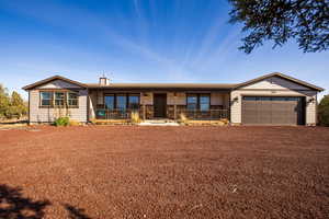 Ranch-style home with covered porch, a chimney, an attached garage, and driveway
