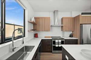 Kitchen with modern cabinets, appliances with stainless steel finishes, wall chimney range hood, open shelves, and light stone counters