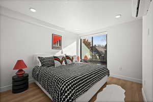 Bedroom with light wood-type flooring, a wall mounted AC, and recessed lighting