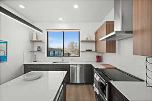 Kitchen with appliances with stainless steel finishes, open shelves, wall chimney exhaust hood, modern cabinets, and light stone countertops