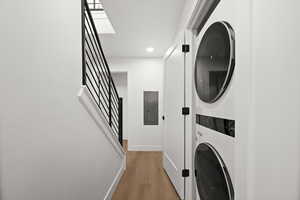 Laundry room featuring electric panel, light wood finished floors, stacked washer / dryer, and recessed lighting