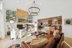 Living room with recessed lighting, light wood finished floors, a fireplace, a towering ceiling, and a chandelier