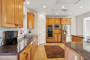 Kitchen with dark stone countertops, stainless steel appliances, light wood finished floors, recessed lighting, and brown cabinets