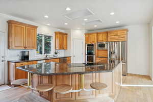 Kitchen with light wood-style flooring, appliances with stainless steel finishes, a kitchen breakfast bar, dark stone counters, and recessed lighting