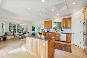 Kitchen featuring dark stone countertops, light wood-style floors, hanging light fixtures, a center island, and brown cabinets