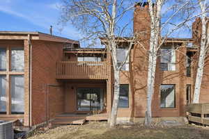 Rear view of house with a balcony, brick siding, and a wooden deck