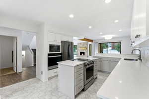 Kitchen featuring stainless steel appliances, a stone fireplace, decorative backsplash, a center island, and white cabinets