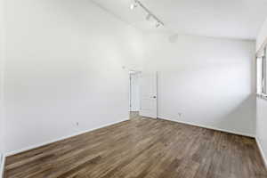 Unfurnished room with rail lighting, hardwood / wood-style floors, and a towering ceiling