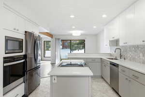 Kitchen featuring appliances with stainless steel finishes, a center island, light countertops, tasteful backsplash, and white cabinetry