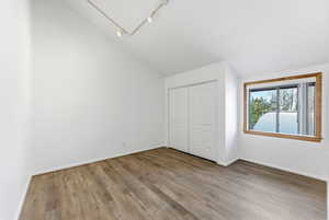 Unfurnished bedroom with light wood-style floors, a closet, high vaulted ceiling, and track lighting