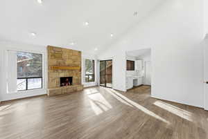 Unfurnished living room featuring high vaulted ceiling, wood finished floors, a stone fireplace, and recessed lighting