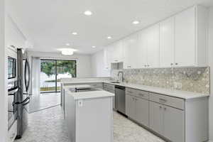 Kitchen featuring tasteful backsplash, appliances with stainless steel finishes, a kitchen island, gray cabinets, and recessed lighting