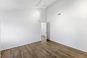Empty room featuring high vaulted ceiling, wood finished floors, and track lighting