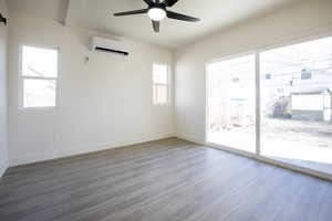 Empty room featuring wood finished floors, a wall unit AC, ceiling fan, and beam ceiling