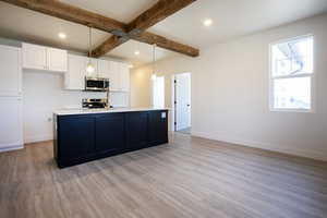 Kitchen featuring white cabinets, pendant lighting, light wood-style floors, a center island with sink, and beam ceiling