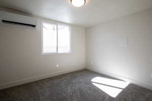 Empty room featuring a wall mounted AC, carpet flooring, and a textured ceiling