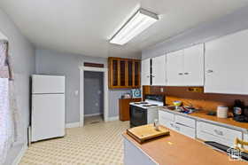 Kitchen featuring white cabinets, freestanding refrigerator, light countertops, electric range oven, and glass insert cabinets