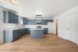 Kitchen with a kitchen island, light wood finished floors, stainless steel appliances, decorative light fixtures, and blue cabinets