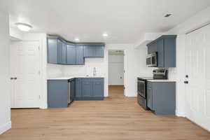 Kitchen featuring blue cabinets, light countertops, stainless steel appliances, light wood-style floors, and recessed lighting