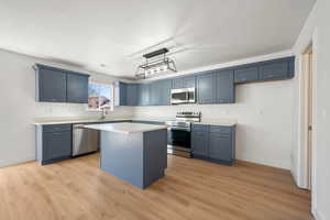 Kitchen featuring appliances with stainless steel finishes, a kitchen island, light countertops, light wood-style flooring, and blue cabinetry