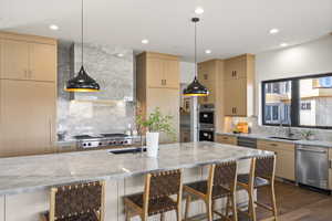 Kitchen with light brown cabinetry, decorative light fixtures, light stone counters, stainless steel appliances, and recessed lighting