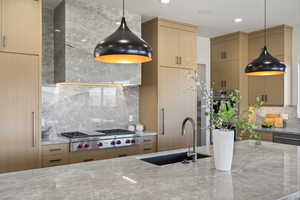 Kitchen with tasteful backsplash, decorative light fixtures, light stone countertops, appliances with stainless steel finishes, and wall chimney range hood