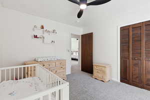 Bedroom featuring a nursery area, light carpet, a closet, and ceiling fan