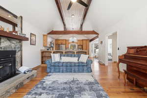 Living area featuring light wood-style floors, a fireplace, beam ceiling, a ceiling fan, and high vaulted ceiling