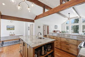 Kitchen featuring pendant lighting, a center island with sink, light stone countertops, light wood-type flooring, and brown cabinetry