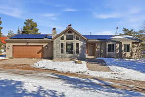 View of front of home featuring solar panels, stone siding, an attached garage, a chimney, and driveway