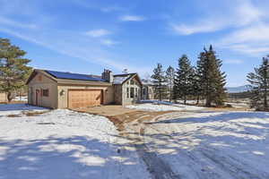 Rustic home with solar panels, a chimney, an attached garage, and a metal roof
