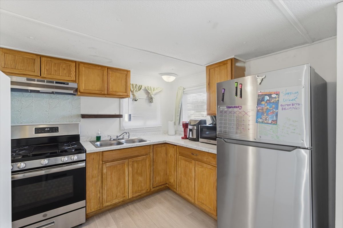 Kitchen featuring stainless steel appliances, light countertops, brown cabinetry, and under cabinet range hood