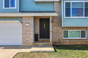 Doorway to property featuring a garage, brick siding, and a shingled roof